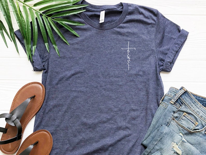May include: A navy blue t-shirt with a white cross and the word "faith" written vertically on the front.