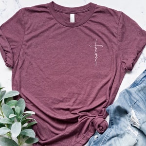 May include: A maroon t-shirt with a white cross and the word "faith" written vertically on the left side of the chest.