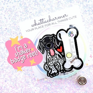 May include: A black and white German Shorthaired Pointer dog badge reel with a bone-shaped charm. The charm has the text "whattacharmer" on it. The badge reel has a pink and yellow star sticker with the text "I'm a shaker badge reel!" on it.