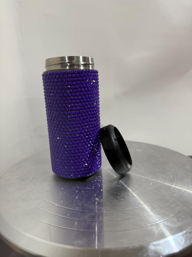May include: A purple travel mug with a stainless steel lid and a sparkly purple finish. The mug is sitting on a silver surface.