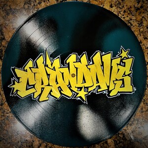 May include: A black vinyl record with a yellow graffiti design that says "Graffiti" on it.