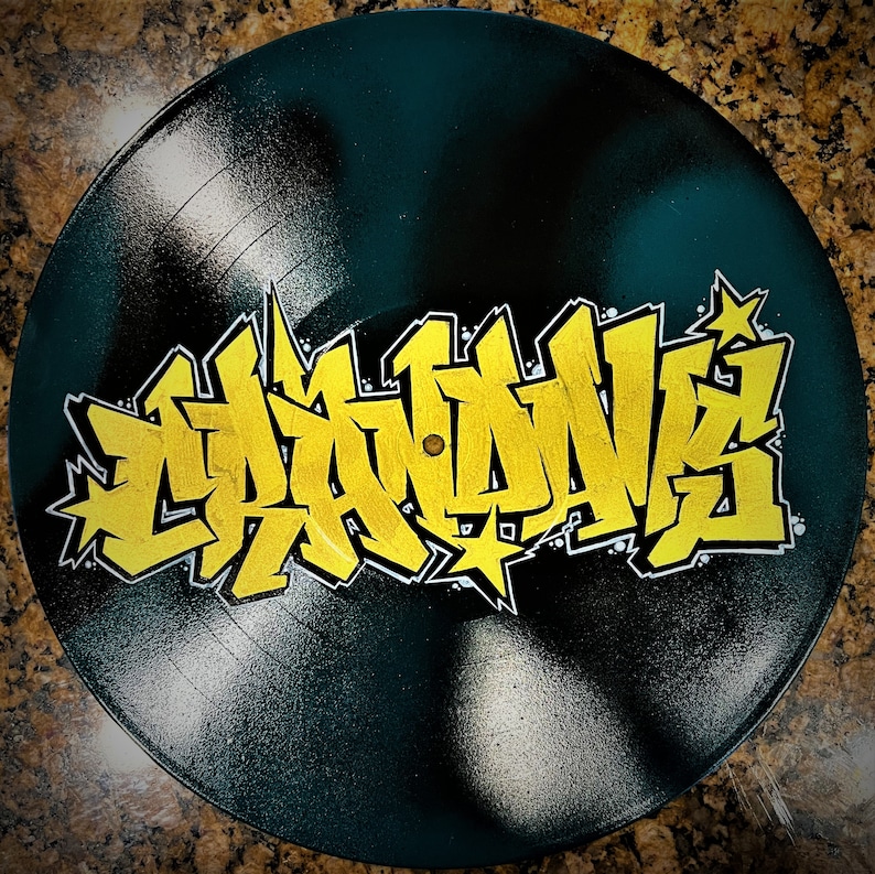 May include: A black vinyl record with a yellow graffiti design that says "Graffiti" on it.