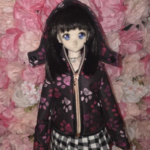 May include: A black hooded jacket with a pink paw print pattern. The jacket has a gold zipper and a black and white plaid skirt.