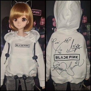 Könnte beinhalten: Weißer Hoodie mit schwarzem Text "BLACKPINK" und schwarzen Kordelzugbändern. Der Hoodie hat schwarze Unterschriften auf der Rückseite.