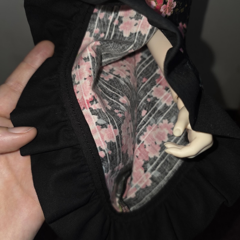 May include: Black dress with a ruffled hem, displaying a floral lining with pink blossoms on a black and white striped pattern. The dress is held open, revealing the interior design.