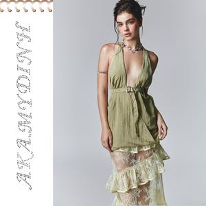 Puede incluir: Una mujer lleva un vestido verde de tirantes con una falda de encaje superpuesta. El vestido tiene un cinturón y un cierre de botón. La mujer lleva un collar.