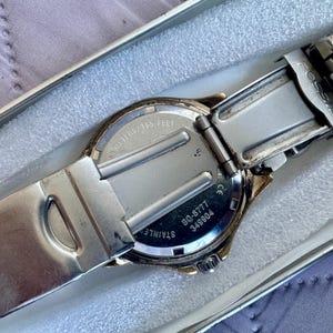 May include: A silver-tone Fossil wristwatch with a stainless steel link bracelet. The back of the watch case displays the text BQ-8777, 349904, and 50 meters/165 feet. The watch is shown from the back, revealing the metal clasp and casing.