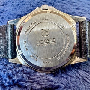 K&ouml;nnte beinhalten: Nahaufnahme der R&uuml;ckseite einer Wenger SAK Design Uhr. Die Uhr hat einen Edelstahlr&uuml;cken mit dem Markennamen und Logo. Die Uhr ist bis 100 m wasserdicht und hat ein schwarzes Lederarmband.