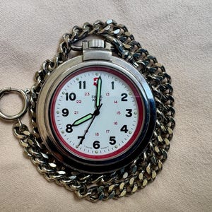 May include: A silver Swiss Army pocket watch with a white face, black numerals, and a red inner ring. The watch has a chain and a ring for attaching to clothing. The watch hands are black and glow in the dark.