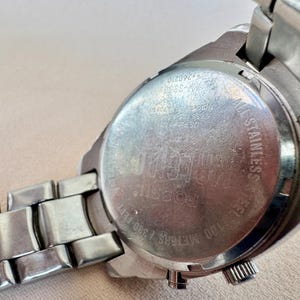 May include: Close-up of a silver-toned Fossil watch. The watch features a stainless steel back with the brand name and other details. The watch band is also silver-toned and made of metal links. The watch is water resistant up to 100 meters / 330 feet.