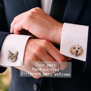 Puede incluir: Gemelos con retratos de mascotas pintados a mano. Uno muestra la cara de un gato, el otro la de un perro. Los gemelos plateados están colocados sobre puños de camisa blancos, que se llevan con un traje oscuro.