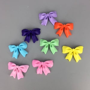 May include: Assortment of nine colorful bows in various colors including purple, blue, green, yellow, orange, and pink. The bows are made of a soft, pliable material and are perfect for adding a touch of whimsy to crafts, gifts, or decorations.