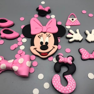 May include: Pink and black fondant cake topper featuring a Minnie Mouse character with a pink bow, a pink polka dot bow, a pink purse, two white gloves, two pink shoes, and a pink polka dot number 3.