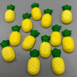 May include: A collection of 14 yellow pineapple shaped cake decorations with green leaves.