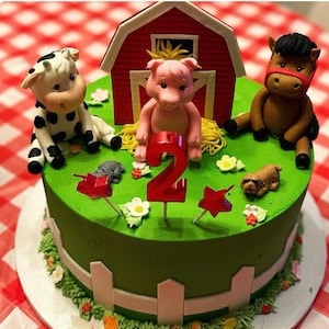 May include: A green and white two-tiered cake decorated with farm animals, a red barn, and a number two candle. The cake is on a white cake stand.