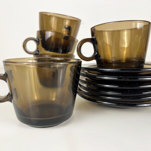 K&ouml;nnte beinhalten: Satz mit sechs braunen Kaffeetassen und Untertassen aus Glas. Die Tassen haben eine abgerundete Form und einen Henkel. Die Untertassen sind rund und haben einen leicht erh&ouml;hten Rand.