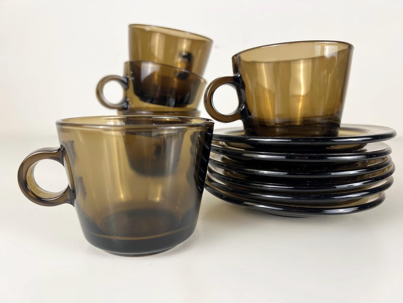 K&ouml;nnte beinhalten: Satz mit sechs braunen Kaffeetassen und Untertassen aus Glas. Die Tassen haben eine abgerundete Form und einen Henkel. Die Untertassen sind rund und haben einen leicht erh&ouml;hten Rand.