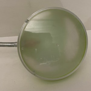 May include: A silver desk lamp with a green glass shade. The lamp has a flexible arm and a round base.