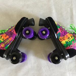 May include: A pair of black roller skates with purple wheels. The skates have a colorful, abstract design with green laces. The design includes a piano keyboard, a skull, and the word "Jacks".