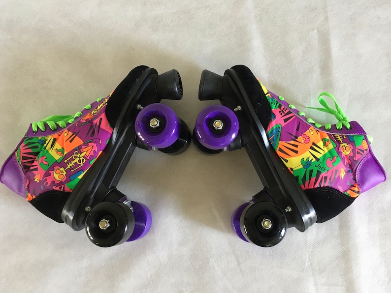 May include: A pair of black roller skates with purple wheels. The skates have a colorful, abstract design with green laces. The design includes a piano keyboard, a skull, and the word "Jacks".