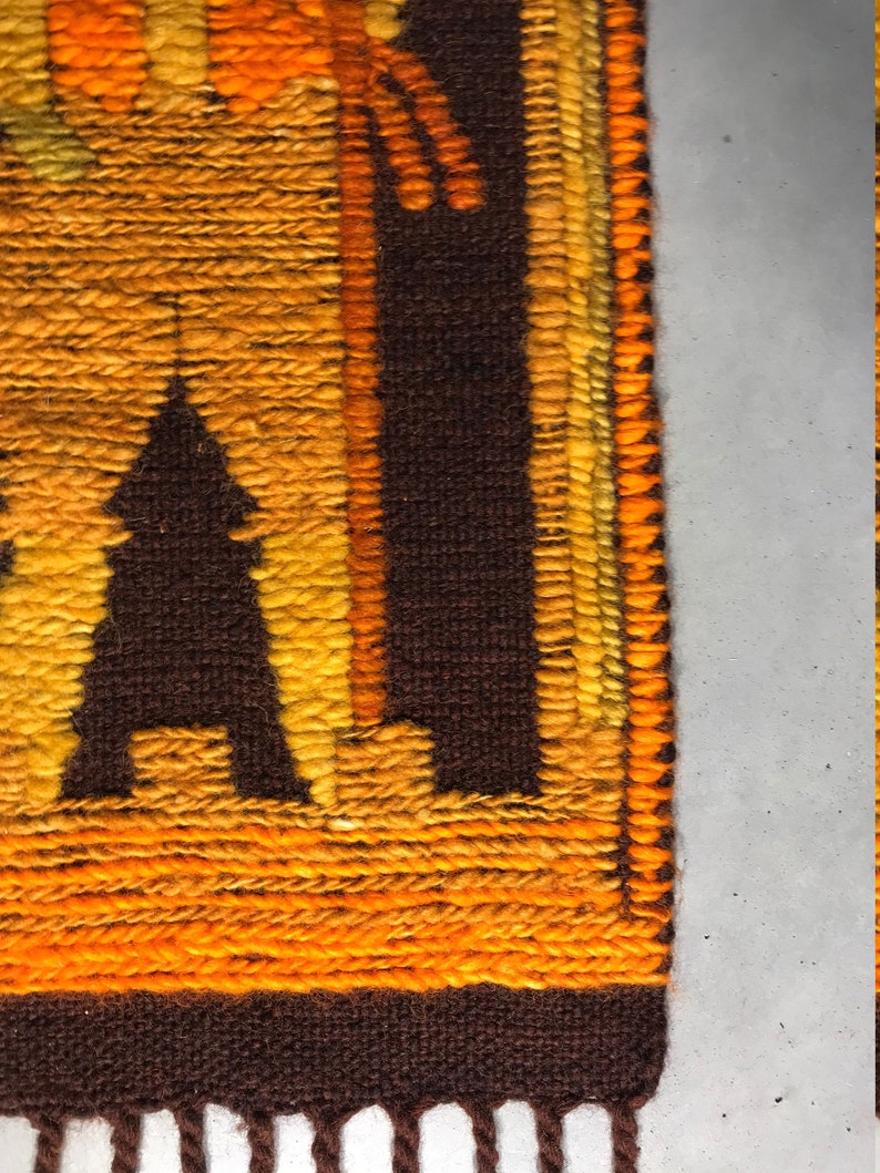 May include: A brown and orange woven wall hanging with a geometric pattern. The hanging has a fringe at the bottom.