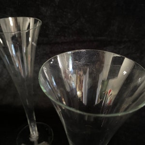 May include: Two clear glass champagne flutes with a tall, narrow design. The flutes are empty and have a smooth, polished surface.