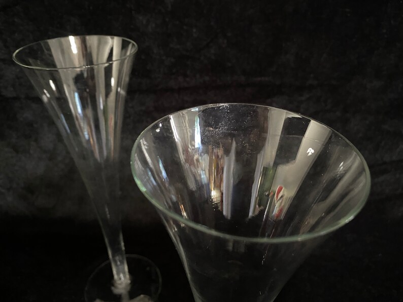 May include: Two clear glass champagne flutes with a tall, narrow design. The flutes are empty and have a smooth, polished surface.
