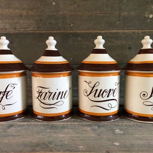 Op de afbeelding: Set van vier keramische potten met bruine, witte en oranje strepen. Elke pot heeft een ander label: "Cafe", "Farine", "Sucre" en "Sel".