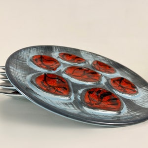 May include: A set of six blue and white ceramic plates with red and black designs. The plates have six individual indentations, each with a different design.