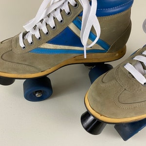 May include: A pair of vintage roller skates with brown suede uppers, blue and white accents, and white laces. The skates have black and blue wheels.