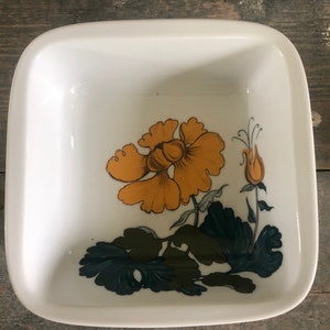 May include: White square ceramic dish with rounded corners. The dish features a floral design with an orange flower, green leaves, and a small orange bud. The dish is likely vintage and suitable for serving food.
