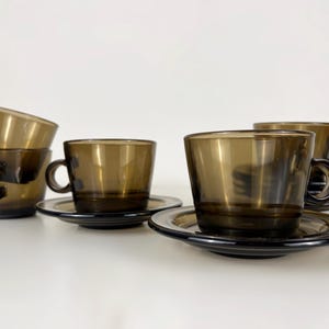 K&ouml;nnte beinhalten: Satz mit sechs braunen Glas-Teetassen und Untertassen. Die Tassen und Untertassen sind &uuml;bereinander gestapelt.