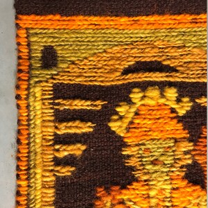 May include: A close-up of a brown, orange, and yellow woven wall hanging with a geometric pattern. The hanging is made of yarn and has a fringe border.