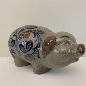 Op de afbeelding: Een keramische spaarpot met een bruin, blauw en wit bloemenmotief. De spaarpot ligt met zijn kop naar de zijkant gedraaid.