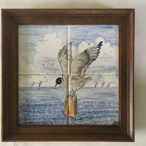 May include: A framed tile depicting a seagull in flight over a blue and white seascape. The seagull is perched on a wooden post with its wings spread. The tile is framed in a dark wood frame.