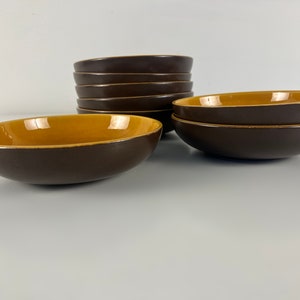 Op de afbeelding: Een set bruine keramische kommen met een contrasterend tan interieur. De kommen hebben een eenvoudig, afgerond ontwerp en een gladde afwerking. De kommen zijn gestapeld en gerangschikt op een wit oppervlak.
