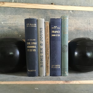 Op de afbeelding: Een set van vijf vintage hardcover boeken met Franse titels, gebruikt als boekenleggers met twee zwarte, ronde, gegroefde objecten.
