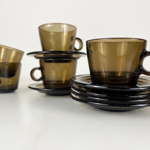 K&ouml;nnte beinhalten: Set aus vier braunen Glas-Teetassen und Untertassen. Die Tassen und Untertassen sind &uuml;bereinander gestapelt.