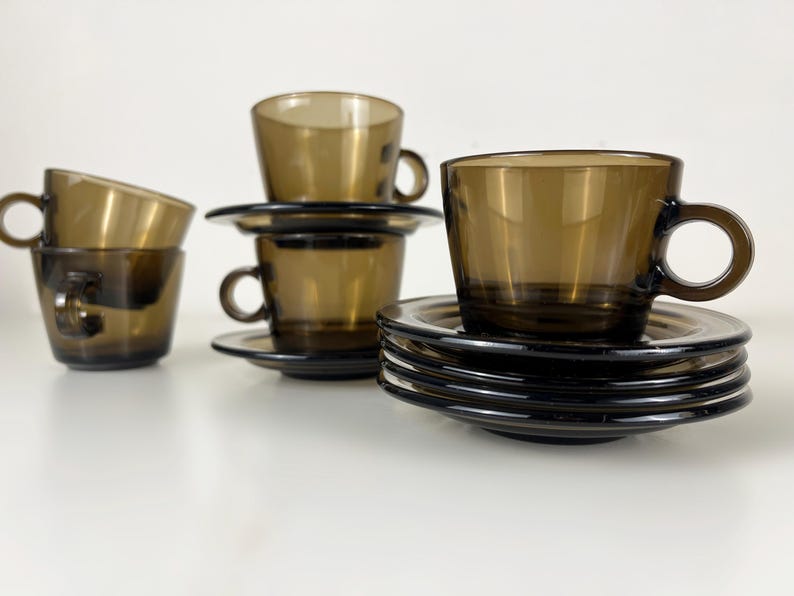 K&ouml;nnte beinhalten: Set aus vier braunen Glas-Teetassen und Untertassen. Die Tassen und Untertassen sind &uuml;bereinander gestapelt.