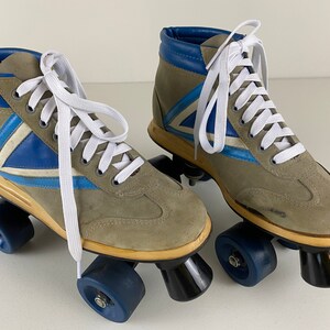 May include: A pair of vintage roller skates with gray suede uppers, blue and white accents, and white laces. The skates have blue wheels and black trucks.