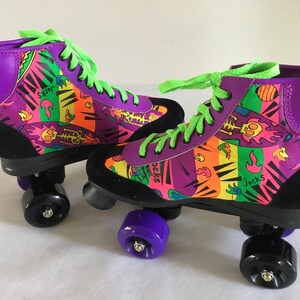 May include: A pair of purple and black roller skates with neon green laces and colorful graphic print featuring flames, skulls, and the word "Jocks".