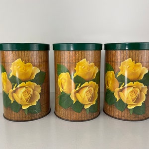 Op de afbeelding: Drie vintage metalen kannen met groene deksels en gele rozenbloemmotieven op een bruine achtergrond.