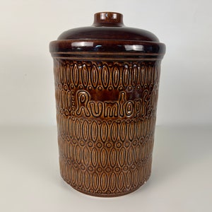 Könnte beinhalten: Eine braune Keramikdose mit Deckel und einem dekorativen Muster. Die Dose ist mit "Rumtopf" beschriftet.