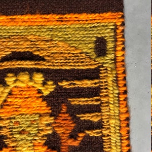 May include: Close-up of a brown, orange, and yellow woven wall hanging with a geometric pattern. The hanging has a fringe border.