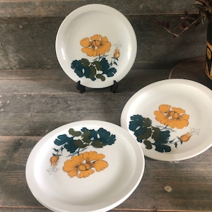 May include: Three white ceramic plates with a floral design. The plates feature yellow flowers with green leaves on a white background.