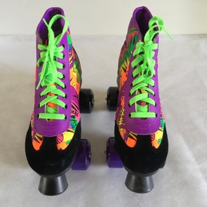 May include: A pair of purple and black roller skates with neon green laces and colorful cartoon graphics. The skates have four wheels each.
