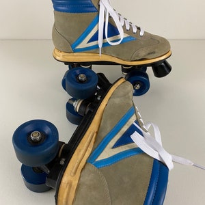 May include: A pair of vintage roller skates with blue and white accents. The skates are made of suede and have a high-top design. The wheels are blue and have a black center.