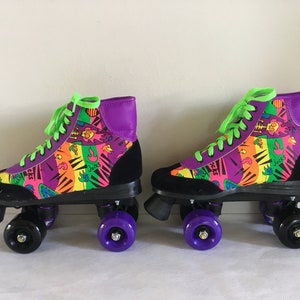 May include: A pair of black and purple roller skates with neon green laces. The skates have a colorful, abstract print with the word "Jack's" on them.