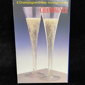 May include: A box of two champagne glasses, labeled "2 Champagner-Gl&auml;ser mundgeblasen CHAMPAGNER". The glasses are clear and have a long, slender stem.