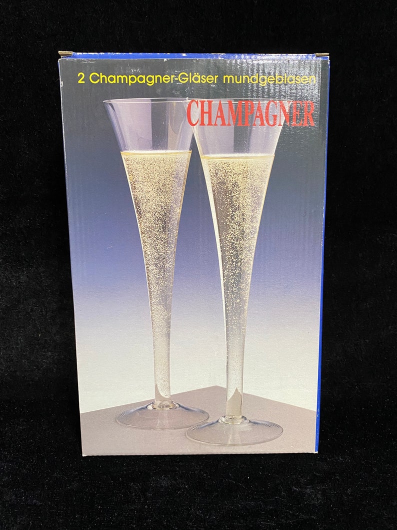 May include: A box of two champagne glasses, labeled "2 Champagner-Gl&auml;ser mundgeblasen CHAMPAGNER". The glasses are clear and have a long, slender stem.